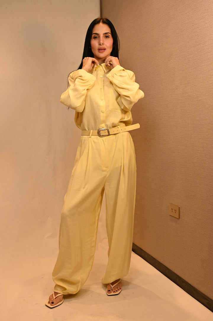 Modelo con camisa safari y pantalón amarillo mantequilla, ajustando el cuello